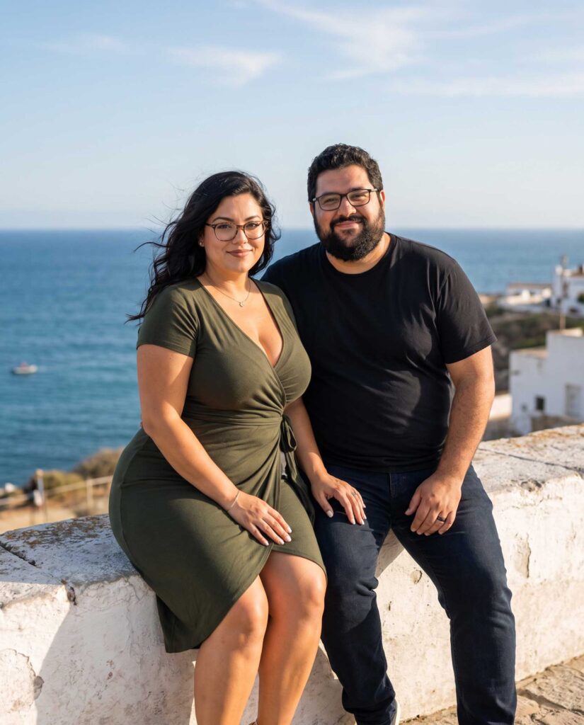 Anna und Karl sitzen gemeinsam auf einer weißen Mauer mit Blick auf das Meer.