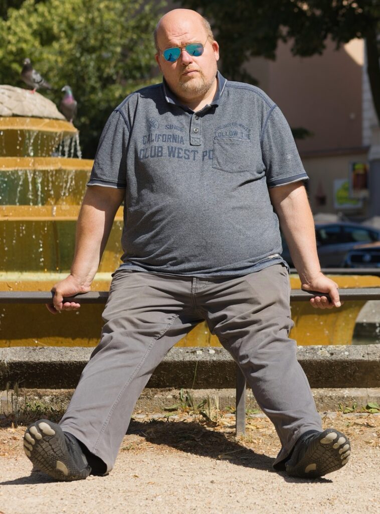 Heiko sitzt mit Sonnenbrille auf einer Bank vor einem Brunnen in Frankfurt-Höchst.