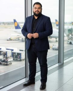 Mark steht im dunklen Anzug vor einer großen Fensterfront am Flughafen Frankfurt.